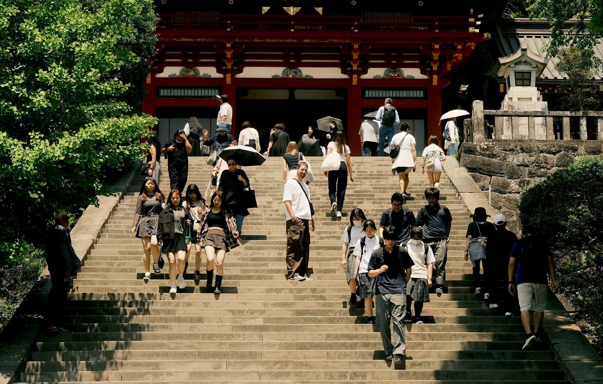 Visitors on the sunlit stone steps below a red shrine gate